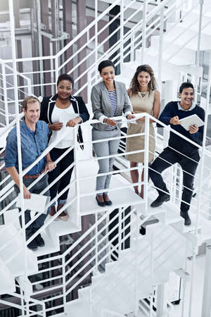United in their quest for success. Portrait of a group of smiling coworkers standing on stairs in a modern office.の写真素材