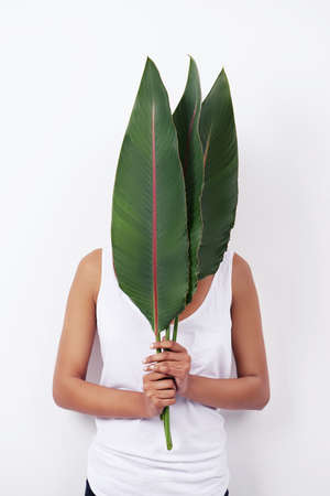 Hidden beauty. Studio shot of an attractive young ethnic woman holding palm fronds in front of her...