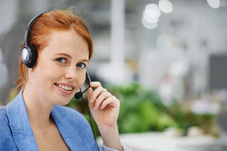 Assistance is a phone call away. Shot of an attractive red headed female wearing head sets in an...
