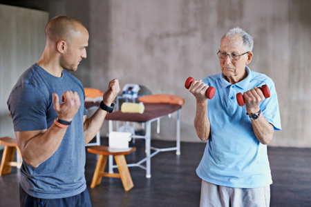 Just give me 2 more. Shot of a physiotherapist helping a senior man with weights.の写真素材