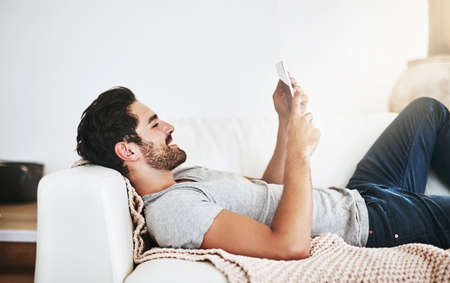 Just me, myself and my device this weekend - Shot of a young man using wireless technology on the sofa at homeの写真素材