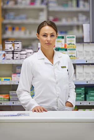 Treatment begins with your local pharmacist. Portrait of an attractive young pharmacist standing at the prescription counter.の写真素材