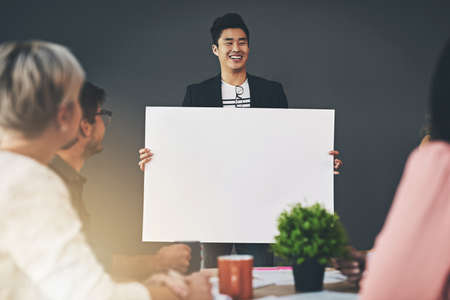 Place your ideas here. Shot of a young businessman holding up a placard during a meeting inside.の写真素材