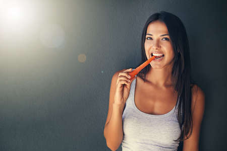 Theyre chock full of vitamins. Shot of a beautiful young woman biting into a carrot.の写真素材