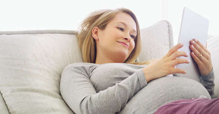 Researching baby facts. Shot of a pregnant woman using a tablet at home.の写真素材