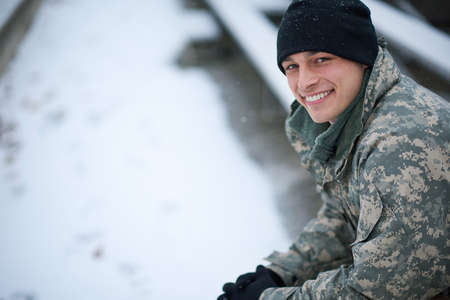 Its cold but I stay committed. Shot of a young soldier sitting outside on a snowy day.の写真素材