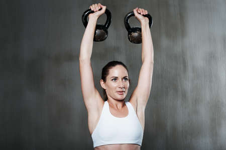 Looking good takes focus and determination. Shot of a woman working out with kettle bells at the...