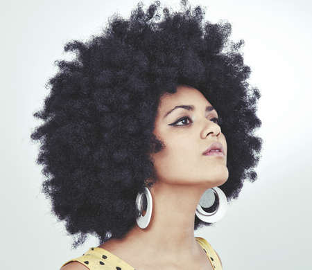 Groovy chick with attitude. Shot of a young woman with an afro wearing a retro outfit posing in...