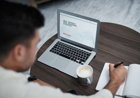 All growth depends on action. Shot of a young man using a laptop and writing in a notebook while...