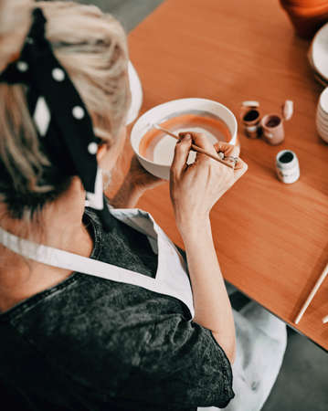 I was created to create. High angle shot of an unrecognizable woman sitting alone and painting a pottery bowl in her workshop.の写真素材