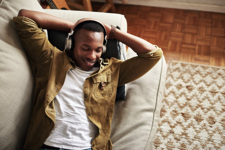 This is a really good song. High angle shot of a handsome young man smiling with his eyes closed while listening to music on his headphones at home.の写真素材