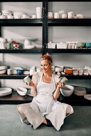 Take your pick. Full length portrait of an attractive mature woman sitting on the floor and holding her pottery in her workshop.の写真素材