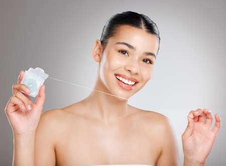 Its dentist recommended. Studio shot of an attractive young woman flossing her teeth against a grey...