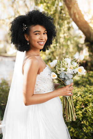Im ready to say I do. Portrait of a happy and beautiful young bride holding a bouquet of flowers while posing outdoors on her wedding day.の写真素材