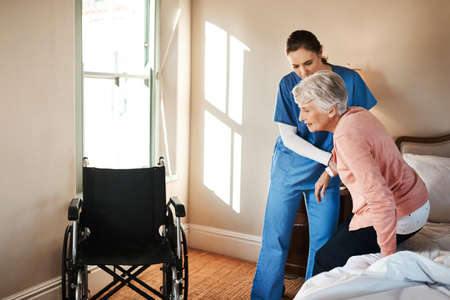 Simple movements arent so simple anymore. Shot of a young nurse helping a senior woman get up from...