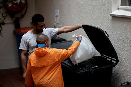 Healthy relationship , healthy lifestyle. Shot of a father and son putting newspaper in the bin to...