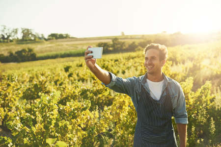 Check out my crops. Shot of a young man taking a selfie with his cellphone while working on a farm.