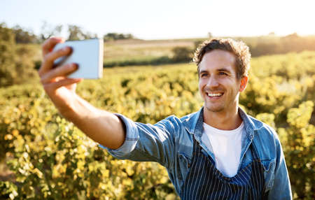 Im proud of my efforts. Shot of a young man taking a selfie with his cellphone while working on a farm.の写真素材
