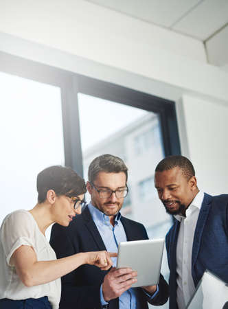 Teamwork and technology - invaluable business assets. Shot of a team of colleagues using a digital...