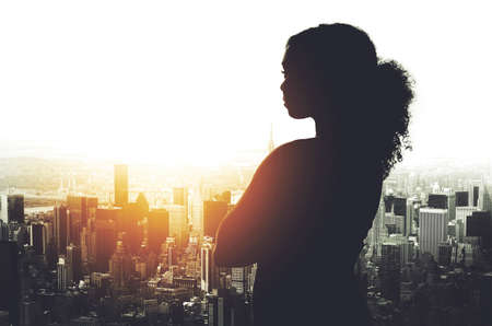 Her success has been shaped in this city. Silhouetted shot of a young businesswoman looking at a cityscape from an office window.の写真素材