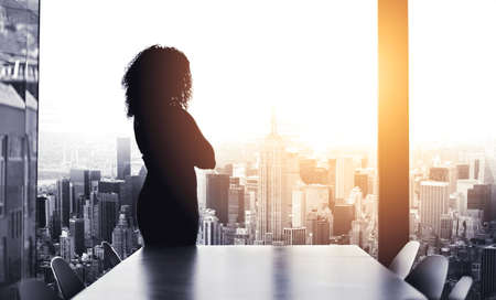 Shes got big plans to run the city. Silhouetted shot of a young businesswoman looking at a cityscape from an office window.の写真素材