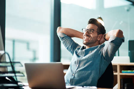 Beating the deadline like the champ he is. Shot of a young businessman taking a break at his desk in a modern office.の写真素材