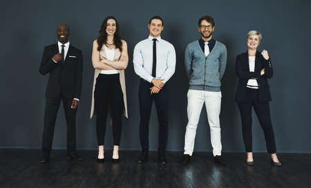 Perfectly suited to the corporate world. Studio portrait of a group of businesspeople standing against a grey background.の写真素材