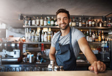 Drinks on me. Portrait of a confident young man working behind a bar counter.の写真素材