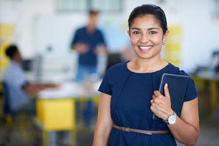 My handheld office. Portrait of an attractive young businesswoman holding a digital tablet while standing in her office.の写真素材