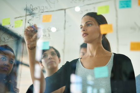Planning is the first step. Cropped shot of a group of young designers planning on a glass board.
