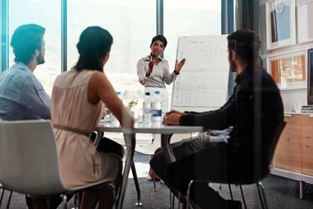 Explaining her plan in detail. Shot of a businesswoman giving a whiteboard presentation to a group of colleagues in a boardroom.の写真素材