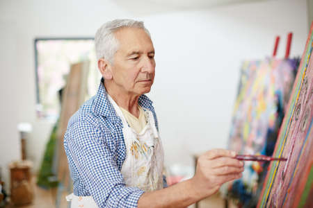 The creative adult is the child who survived. Shot of a senior man working on a painting at home.の写真素材