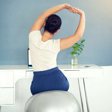 Keep the blood flowing. Rearview shot of a young businesswoman stretching while working at home.の写真素材