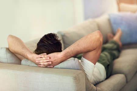 Feet up, wind down. rearview shot of a young man relaxing on the sofa at home.