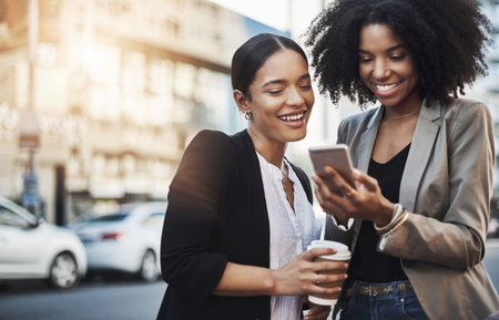 Good news just came in from the office for us. Shot of two businesswomen looking at something on a cellphone in the city.の写真素材