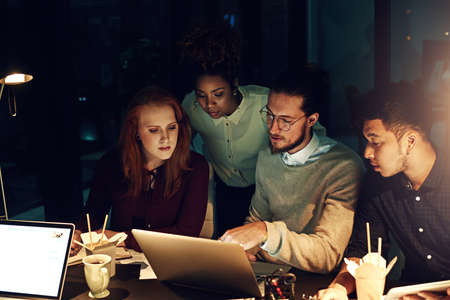 Were committed to completing prioritised tasks. Cropped shot of a group of young people working late in the office.の写真素材