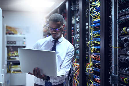 The man with the plan. Cropped shot of a IT technician working on his laptop while standing inside...