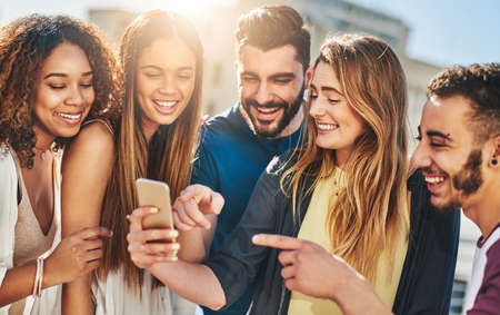 Look at this funny video online. Shot of young friends using a smartphone outside.
