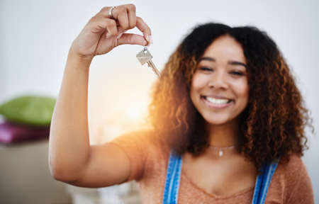 Proper start of adulthood. Cropped shot of a beautiful young woman holding house keys in her new home.の写真素材