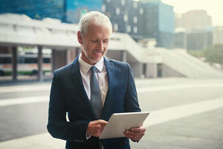 Im loving my new gadget. Shot of a confident businessman using his tablet while standing outside his...