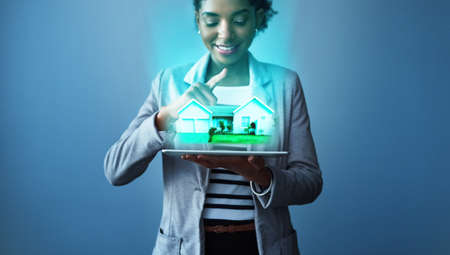 Your perfect home is just an app away. Studio shot of a young businesswoman using a digital tablet with property graphics against a blue background.の写真素材