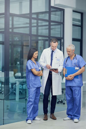 Comparing diagnosis. Shot of a group of doctors talking together over a digital tablet while...