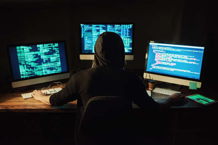 Unraveling the code. Rearview shot of a young hacker cracking a computer code in the dark.