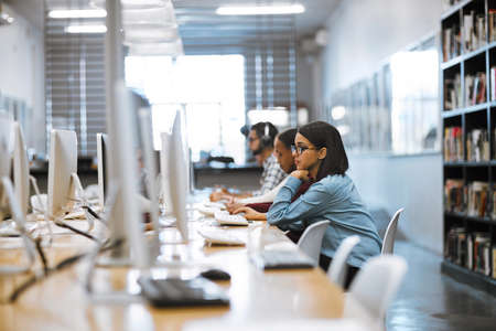 The student life. Shot of a group of university students working on computers in the library at...