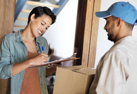 Just sign and the package is yours. Shot of a young woman standing at her front door signing for a...
