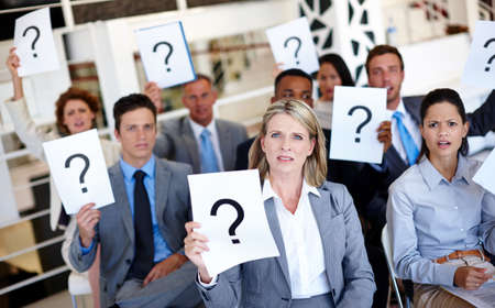 Stop leaving us in the dark. Shot of a group of businesspeople holding up signs with question marks on them during a work presentation.の写真素材