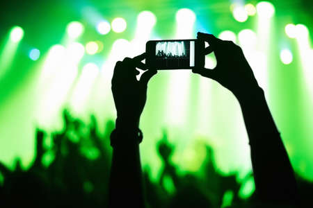 A person filming their favorite band with a camera phone. This concert was created for the sole purpose of this photo shoot, featuring 300 models and 3 live bands. All people in this shoot are model released.の写真素材