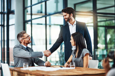 We look forward to having you with us. Shot of businessmen shaking hands during a meeting in a modern office.の写真素材