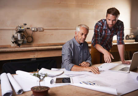 Passing along all his knowledge. Cropped shot of a father and son working together in their workshop.の写真素材