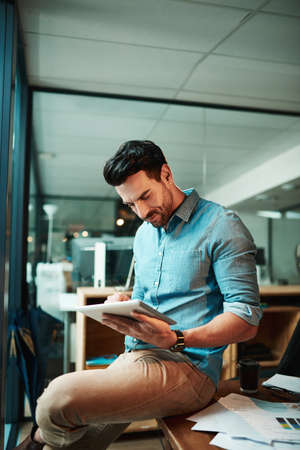 Business, he does it digitally. Shot of a young businessman using a digital tablet in a modern office.の写真素材